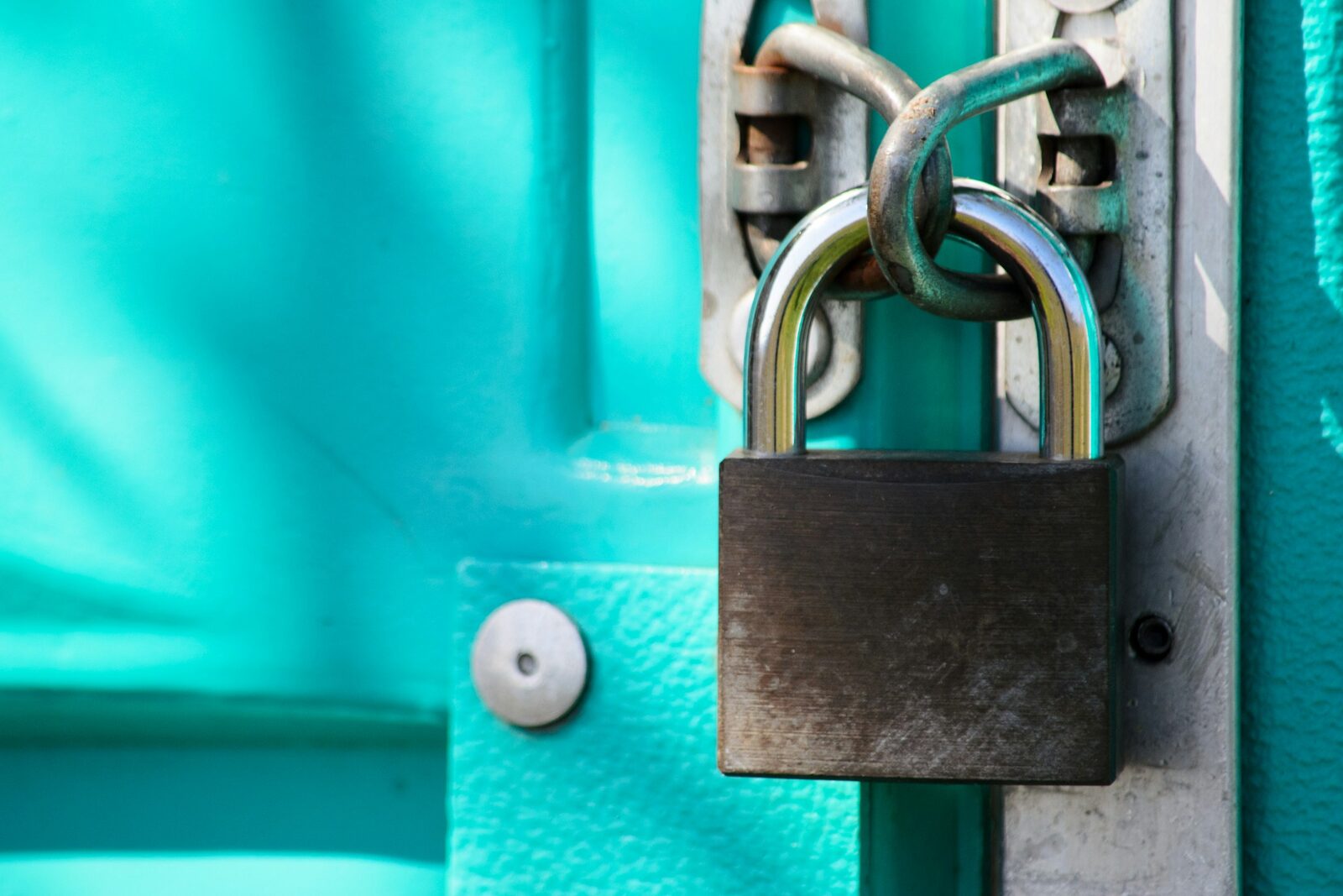Close-up photograph of a metal padlock on a door, in a cool blue tone.